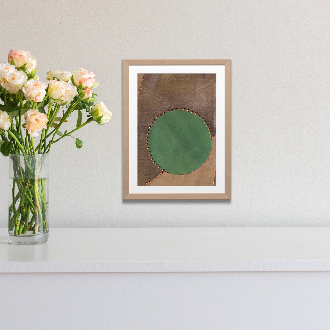 Framed artwork with a green circle on a brown background next to a vase of flowers.