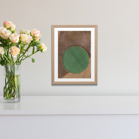 Framed artwork with a green circle on a brown background next to a vase of flowers.