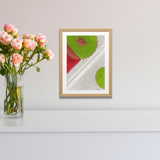Framed abstract artwork with geometric design on a white wall next to a vase of flowers.