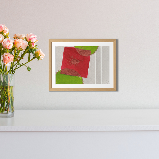 Framed artwork on a wall with a vase of flowers to the left.