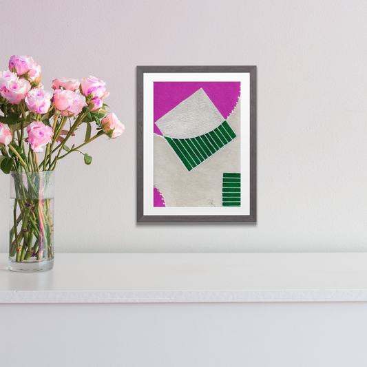 Framed abstract art with pink and green design on a white wall next to a vase of pink flowers.