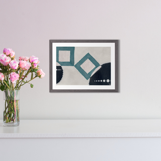 Framed abstract art piece on a wall with a vase of pink flowers next to it.