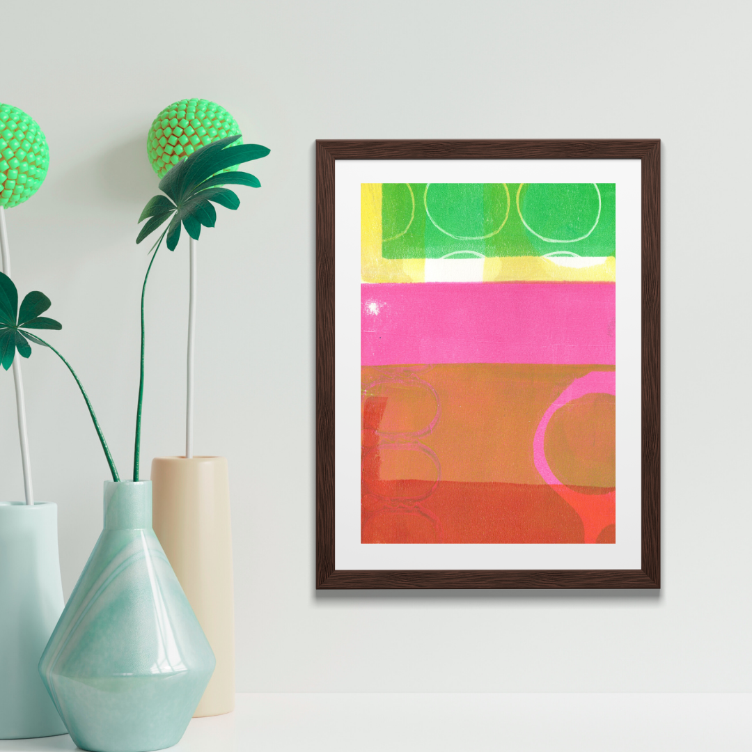 Framed abstract art with colorful geometric design on a wall above a wooden shelf with a plant.