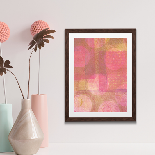 Framed abstract art with pink and orange colors on a wall with decorative vases and plants.