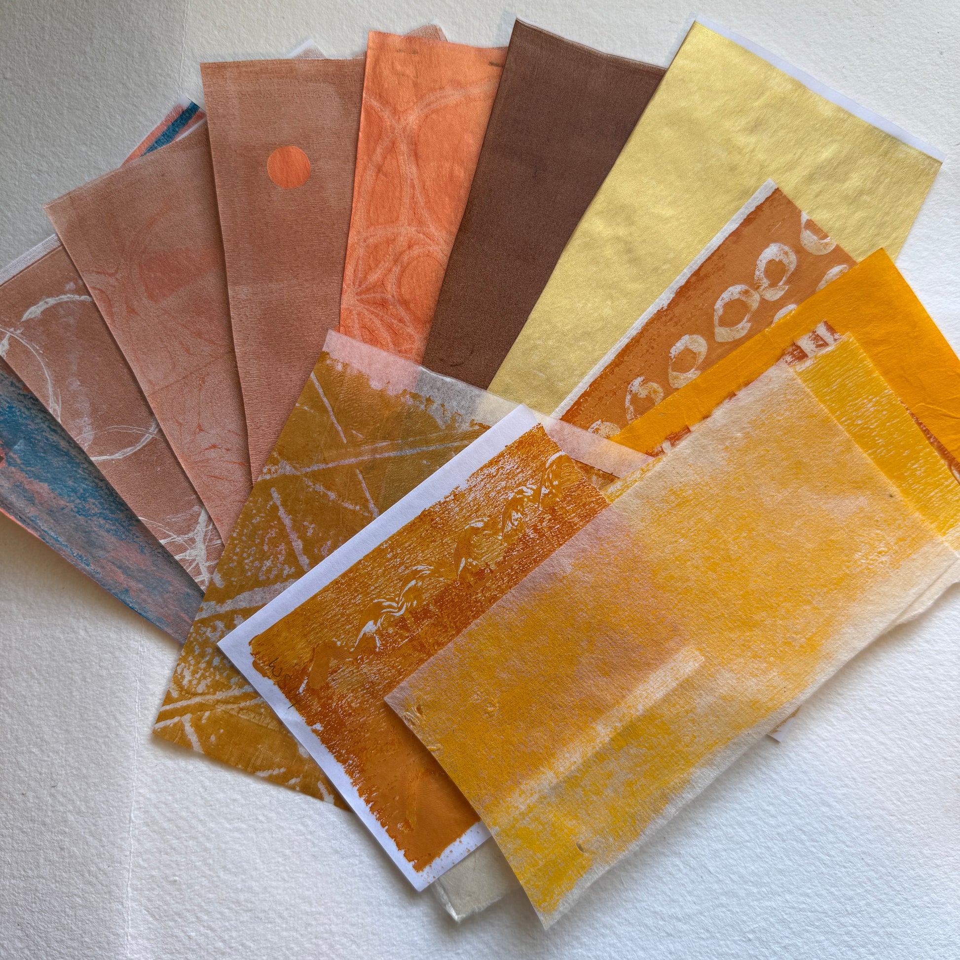 Collection of textured paper samples in orange and  gold on a white background.
